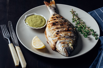 Grilled fish on a plate with lemon sauce and thyme
