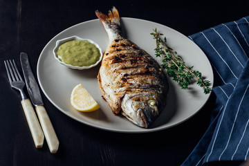 Grilled fish on a plate with lemon sauce and thyme