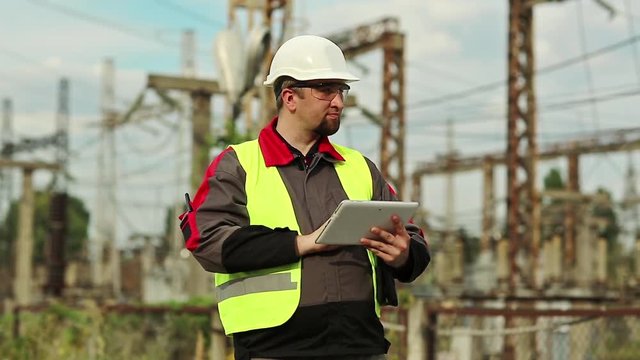 Powerman with tablet computer on power station. Worker in white hard hat on electric power plant, engineering supervision. Factory worker with tablet pc
