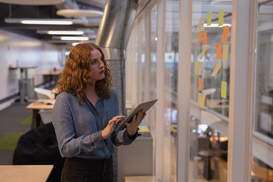 Female Executive Using Digital Tablet While Reading Adhesive Notes In Office