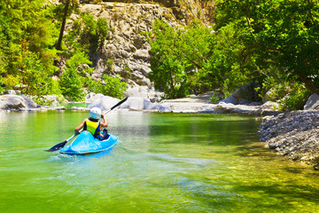 Young unidentified man kayaking along mountain river in summer sunny day