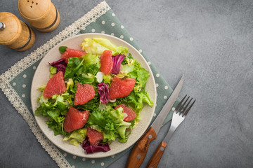 Fresh mix salad with lettuce, green arugula and sliced grapefruit in a plate