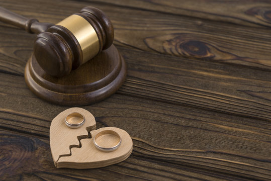 Wedding rings on the figure of a broken heart from a tree, hammer of a judge on a wooden background. Divorce proceedings