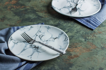 Empty ceramic plate with fork and blue kitchen towel over green concrete table background. Copy space.