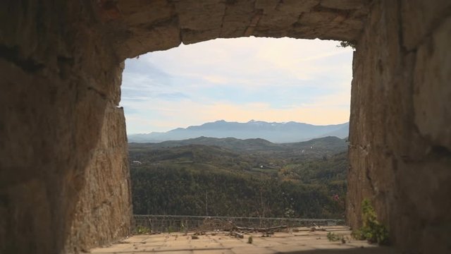 Small breach in the wall of a medieval fortress that shows mountains and woods in the distance, in Abruzzo.