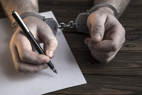 Men's hands with handcuffs fill the police record, confession. on top see the police investigative detective. Arrest, bail, criminal, prison. Close-up
