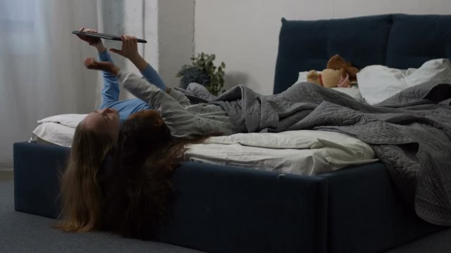 Two cute multiracial little girls using a digital tablet and smiling while lying on their backs on bed in children's room. Lovely multi ethnic kids browsing the net on tablet pc in domestic interior.