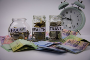 A lot coins in glass money jar on the white background Saving for house, health and travel concept.