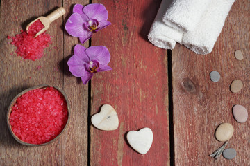 Spa set on red boards with hearts made of stone for massage, bath salt, towels and pink orchid flowers