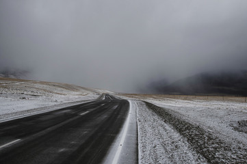 Road asphalt path on a winter snow desert wild mountain valley  at the background of the high peaks under a dramatic storm cloud Chuysky tract Altai Mountains Siberia, Russia