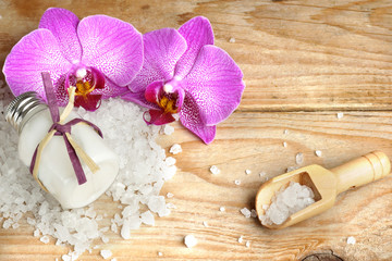 Spa set with body lotion, bath salt, white, pink orchid flower and stones in the form of hearts on wooden background.