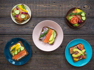 Sandwiches with salmon, black bread and vegetables in plates on the table
