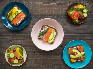 Sandwiches with salmon, black bread and vegetables in plates on the table