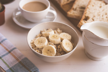 Oatmeal with a banana and coffee with milk for breakfast - close-up, on a light rustic background