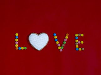 on a red background written in sweets I love in the form of heart cookies with white mastic with multi-colored round candies 