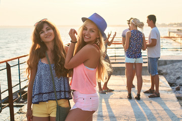 Two beautiful young girls brunette and blonde smiling and having fun at the seaside with group of their friends