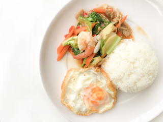 Fried Savory sauteed mixed vegetables with shimp and fried egg served with rice in white dish on white background as Thai homemade meal or recipe in the restaurant. Thai style food.