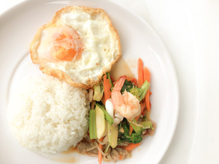 Fried Savory sauteed mixed vegetables with shimp and fried egg served with rice in white dish on white background as Thai homemade meal or recipe in the restaurant. Thai style food.