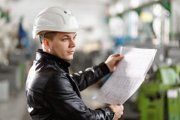 A young successful engineer with a drawing in his hands is standing in the territory of a modern factory. blue toned image