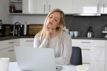 Hübsche blonde Frau sitzt vor ihrem Laptop und überlegt