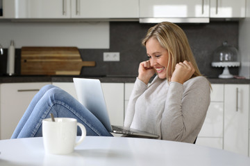 Hübsche blonde Frau mit Laptop auf ihrem Schoß freut sich