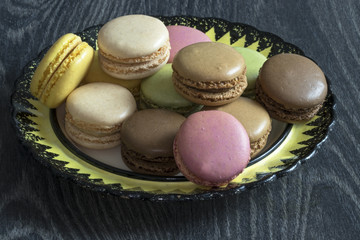 Macarons de couleurs différentes en tas dans une assiette sur fond noir