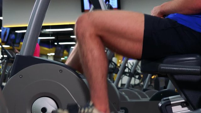 A fit man trains on a recumbent bike in a gym - closeup on legs