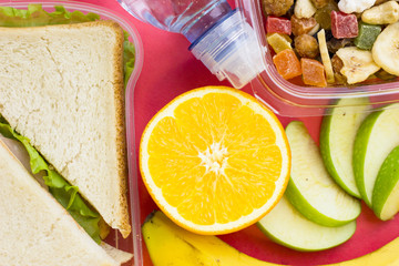 Fresh sandwich with lettuce , orange, banana, slices of green apple and a plastic container of candied fruit, top view, close up, rose background