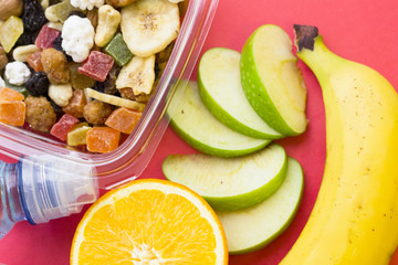 Lemon, banana, slices of green apple and a plastic container of candied fruit, top view, close up, rose background