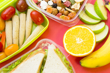 A set of lunch items: sandwich, candied fruit, plastic container with vegetables and fresh fruit, top view, close up, rose background