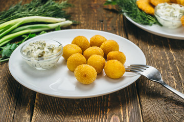 Tasty cheese balls in batter on a white round plate with sauce, parsley and leeks