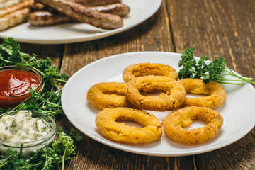 Delicious cheese rings and sausages on a white round plate with ketchup, sauce and parsley