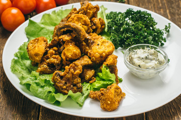 Mushrooms in batter with sauce, parsley, lettuce and tomatoes, on a wooden old table