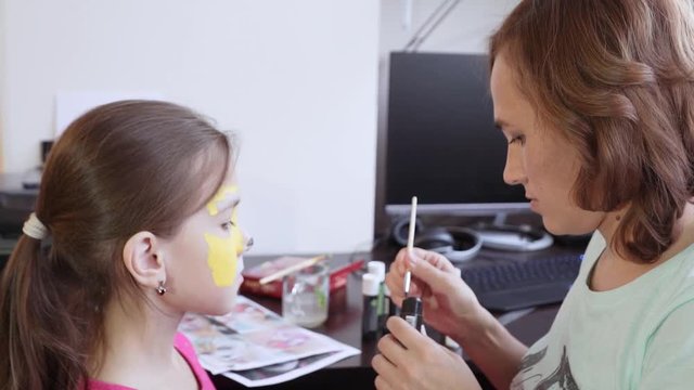 A pretty woman draws on the child's face with a brush. Aquagrim.