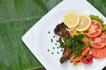Pork steak with fresh pepper serve with corn grilled, tomato grilled and lemon sliced on banana leaf.