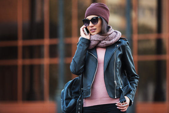 Young fashion woman in black leather jacket using cell phone in city street