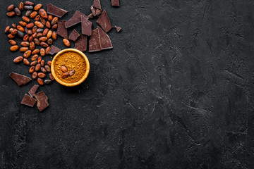 Chocolate and cacao concept. Cocoa powder in bowl near cocoa beans and broken chocolate on black...