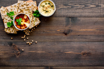 Obraz na płótnie Canvas Serve hummus. Bowl with dish near pieces of crispbread on dark wooden background top view copy space