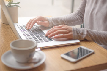 Woman typing on laptop computer and using smart phone 