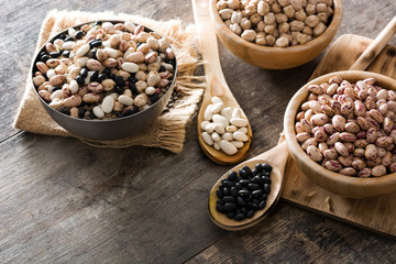 Uncooked assorted legumes in wooden bowl on wooden table