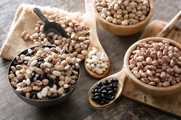 Uncooked assorted legumes in wooden bowl on wooden table