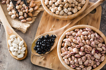 Uncooked assorted legumes top view in wooden bowl on wooden table. Top view