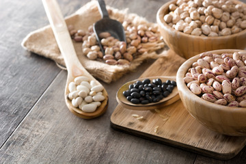 Uncooked assorted legumes in wooden bowl on wooden table. Copyspace