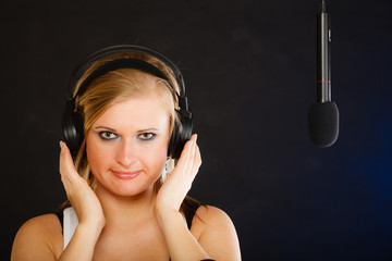 Woman singing to microphone wearing headphones in studio