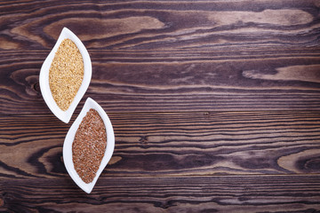Golden and brown flax seeds on dark wooden background.
