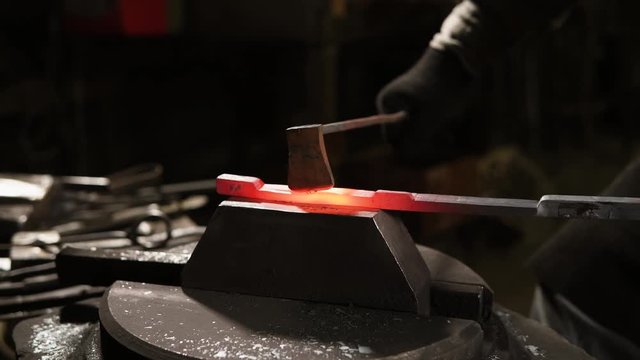 close up shot of the blacksmith's hands, the professional master uses modern equipment to make steel parts, the hammer knocks on the uncoated stripe
