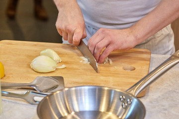 Man cutting an onion with knife on wooden board