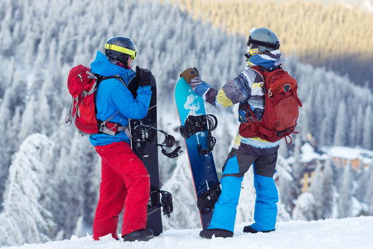 Two snowboarders, with backpacks, stand on the mountain slope