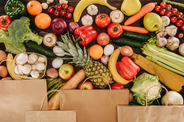 top view of paper bags covering vegetables and fruits on wooden table, grocery concept