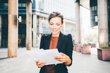 beautiful business woman with paper, dressed in black jacket. Modern building in background.